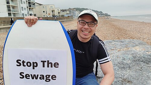 Larry Ngan with "Stop the Sewage" surfboard